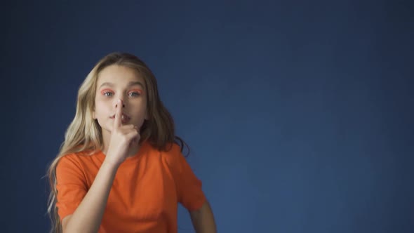 A Young Girl Makes a Gesture of Silence Against a Blue Background