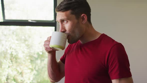 Thoughtful caucasian man is looking out the window and drinking coffee