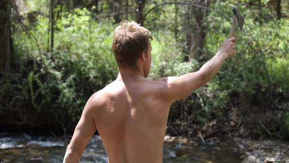 Slow motion shot of a shirtless man practicing his axe throwing skill by trying to throw his hatchet