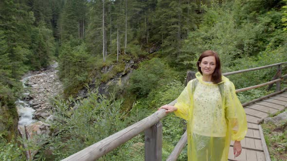 Hiker in a Yellow Raincoat Walks on a Wooden Bridge