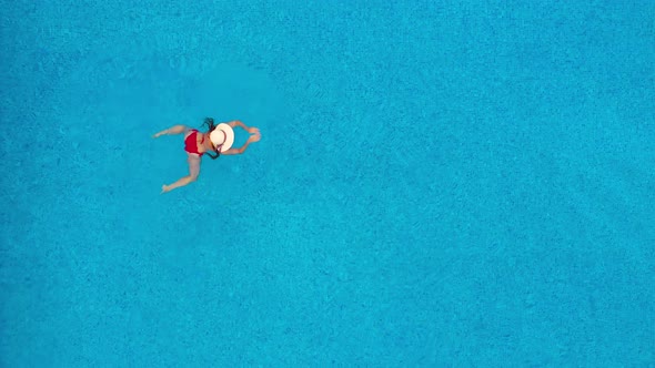 View From the Top As a Woman in Red Swimsuit and Hat Swims in the Pool