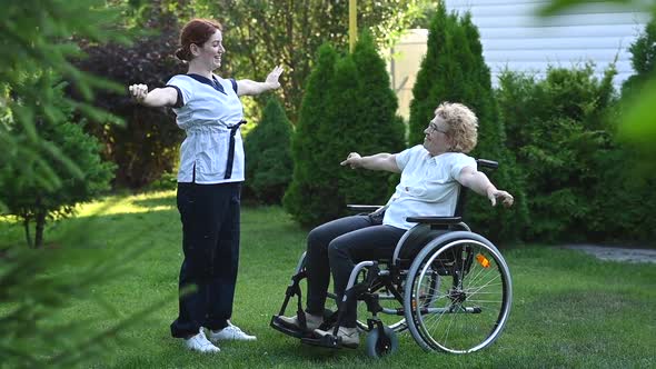 A Nurse is Exercising with an Elderly Patient in a Wheelchair Outdoors