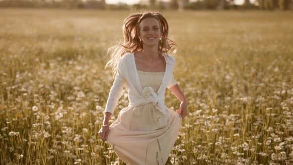 A Happy Woman is Running in Slow Motion Across Field with Camomiles at Sunset