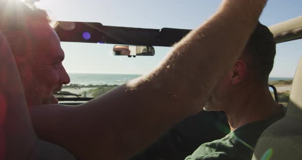 Happy caucasian gay male couple sitting in car and embracing on sunny day at the beach