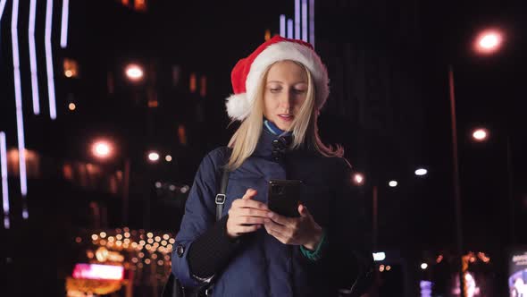 young beautiful blonde in Santa Claus hat, typing message on mobile phone