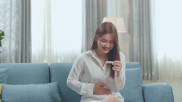 Happy Young Asian Woman Looking At Pregnancy Test And Touching Her Belly