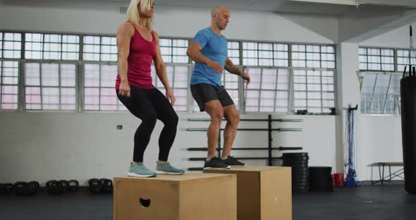 Fit caucasian woman and man jumping on pylo boxes at the gym