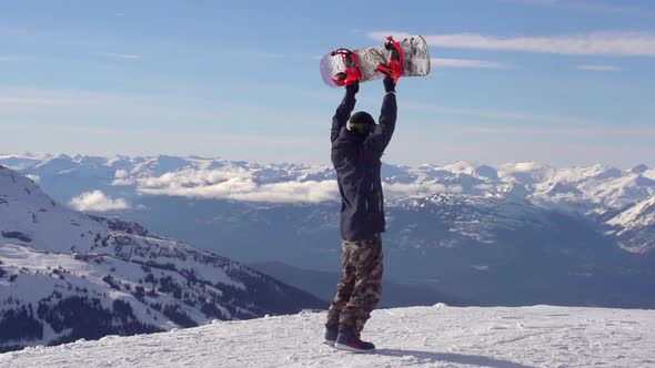 A young man snowboarder standing with his snowboard on a snow covered mountain.