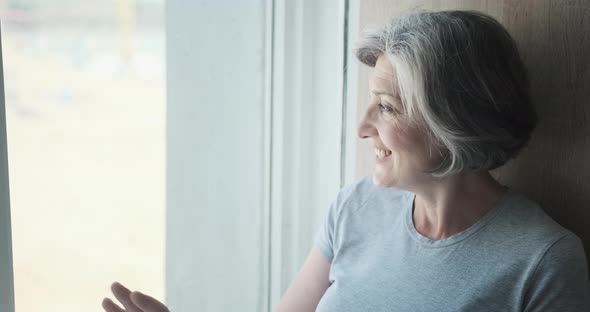 An Elderly Woman Smiling at the Window and Waiting for Her Children