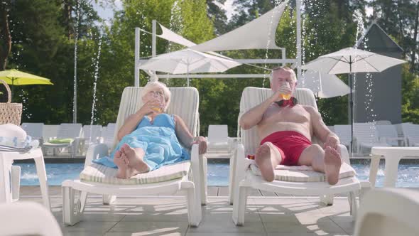 Mature Couple Lying on Sunbeds Near the Pool Drinking Juice, Talking and Smiling