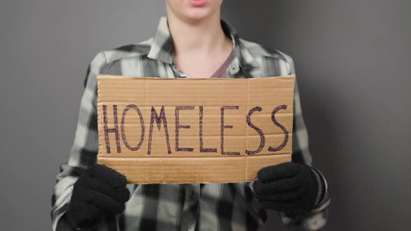 A untidy beggar woman holds a cardboard sign with the inscription homeless.