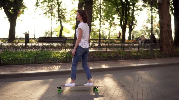 Young Woman in Blue Jeans and White Sneakers Skateboarding at Sunrise in Park