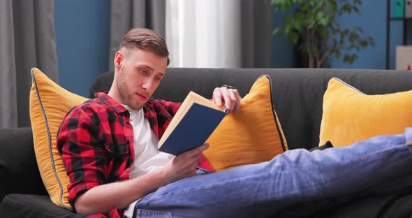 Focused Student Boy Lay Relax on Couch at Home Reading Interesting Book Calm Smiling American