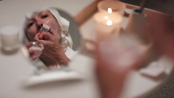 Woman Looking At Mirror Applying Facial Mask