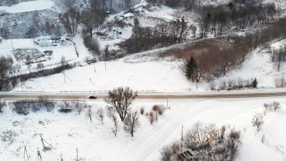 The Car Drives Along a Flat Road in Winter Among the Village  Aerial Side View