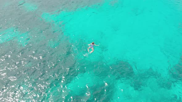 Aerial: woman swimming on turquoise water coral reef tropical caribbean sea