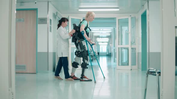 Doctor is Helping a Female Patient to Walk in the Exosuit