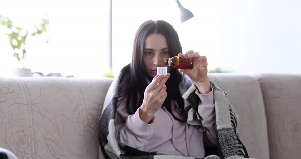 Sick Woman in Plaid Pours Medicinal Syrup on Couch at Home