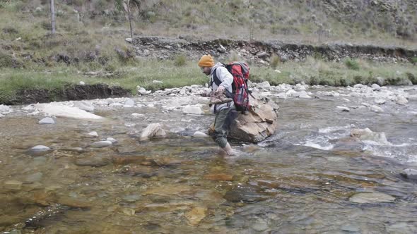 Hiker crossing river bare foot while holding his phone