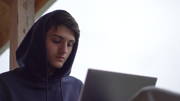 A Young Man is Typing on a Laptop While Sitting on a Terrace Against the Backdrop of a Picturesque