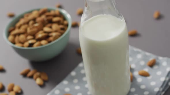 Video of fresh fruit almonds in a bowl and glass bottle of milk on grey background