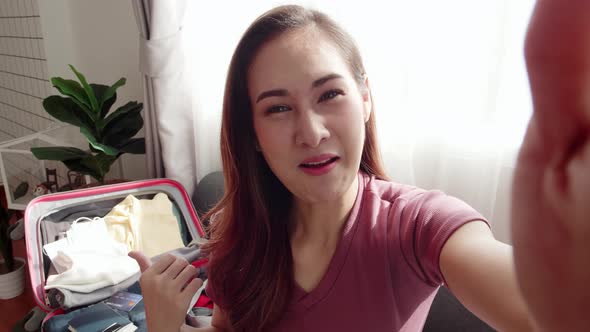 Lovely blogger recording video selfie while packing a suitcase for a travel trip