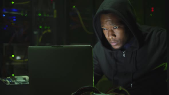 African american male computer hacker using laptop in business server room