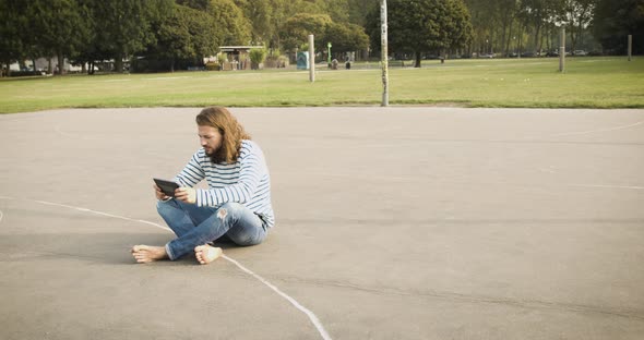 Man sitting on basketball court using digital tablet