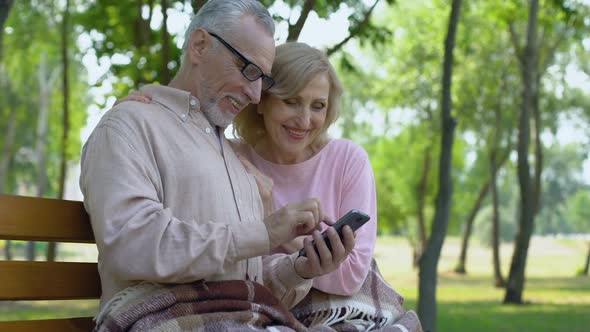 Grandfather and Grandmother Admiring Children Photos in Smartphone Application
