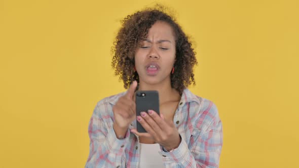 Young African Woman Loss on Smartphone on Yellow Background