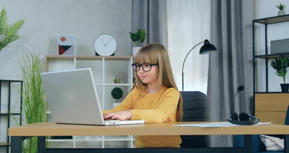 Schoolgirl in Glasses Sitting in front of Computer and Studying Online or doing Hometask at Home