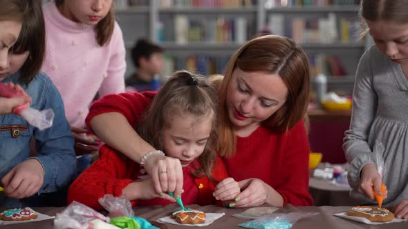 Woman Helping Autistic Girl Icing Cookie in Class