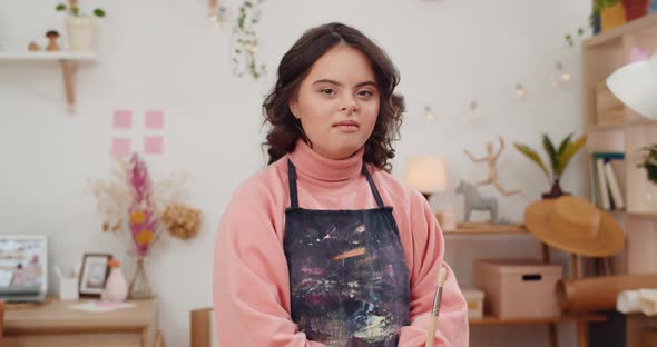 Portrait of Beautiful Girl with Genetic Disorder Wearing in Artists Apron and Holding Paintbrush