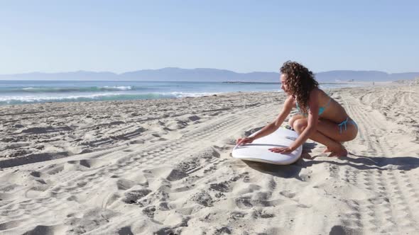 A young woman surfer waxing her board on the beach.