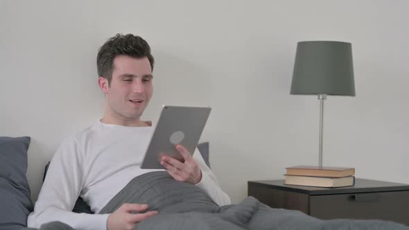 Man Doing Video Call on Tablet While Sitting in Bed