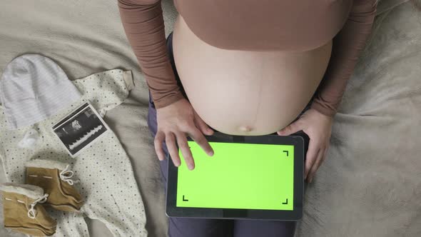 Expecting Pregnant Woman with Large Belly Using Tablet with Chromakey on Bed