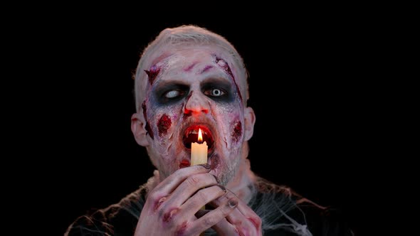Man with Halloween Zombie Bloody Wounded Makeup Trying to Scare Spells Conjures Over a Candle