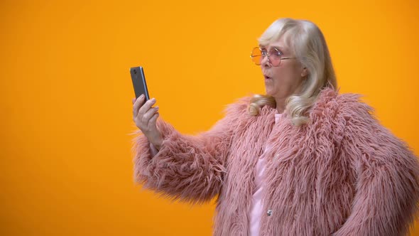 Cheerful Senior Lady in Funny Pink Coat Taking Selfie on Smartphone, Having Fun