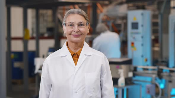 Mature Woman Scientist in Protective Glasses and Lab Coat Standing at Chemical Manufacturing