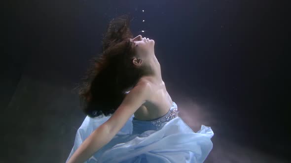 a Beautiful Brunette with Long Hair and a Sequined Dress Is Floating Under the Water. She Throws