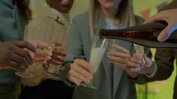 Closeup of Male Hand Pouring Champagne in Glasses During New Year Party in Dark Office