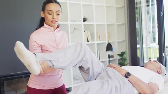 Video of happy biracial female physiotherapist exercising with caucasian senior man