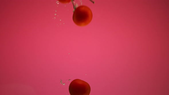 Red Pepper and Tomatoes Falling Into the Water with Bubbles in Slow Motion