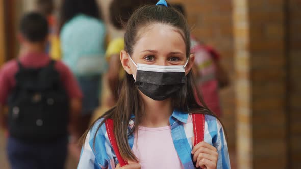 Portrait of caucasian schoolgirl wearing face mask, standing in corridor looking at camera