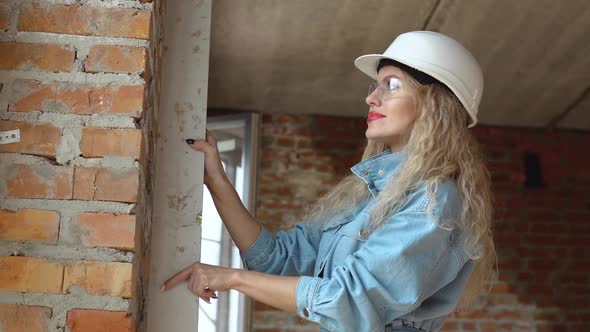 A Female Architect or Bricklayer Stands in a Newly Built House with Untreated Walls and Checks the
