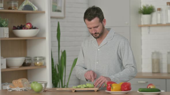 Healthy Young Man Cutting Cucumber in Kitchen