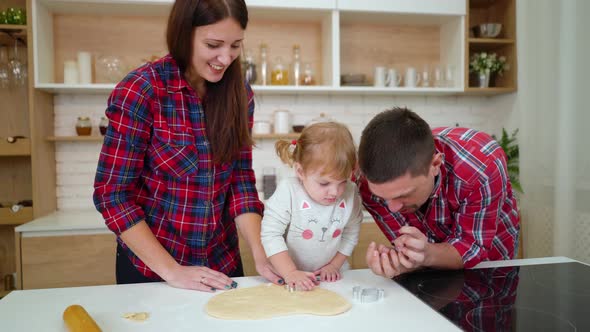 Parents Help their Little Daughter to Cut out Cookies in Kitchen