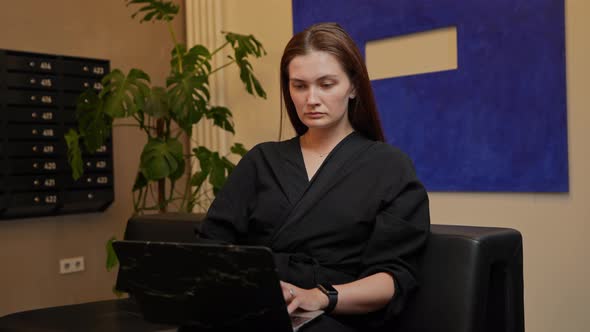 A Woman in a Dress Sits in a Chair Working on a Laptop in the Lobby of the Hotel