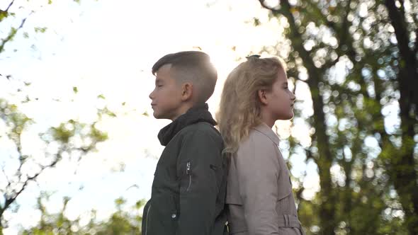 Side View of Happy Boy and Girl Holding Hands While Standing Against Trees at Sundown in Autumn