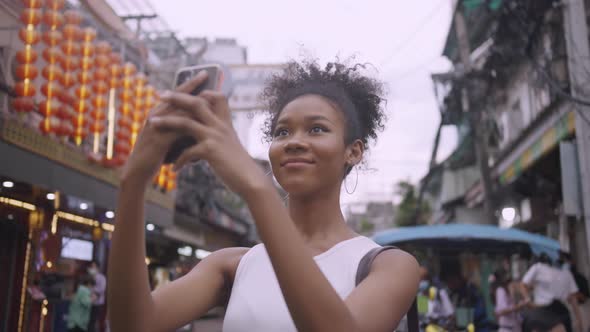 A beautiful woman tourist enjoys taking photos of the city view of Yaowarat Road, Thailand.